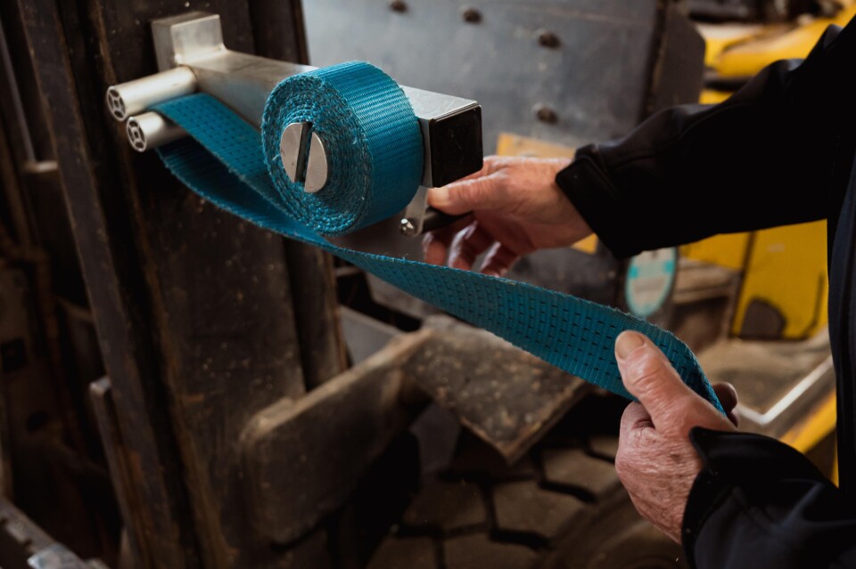 Monteur rolt een oranje spanband op met de aluminium spanbandoproller, bevestigd aan een werkbank.