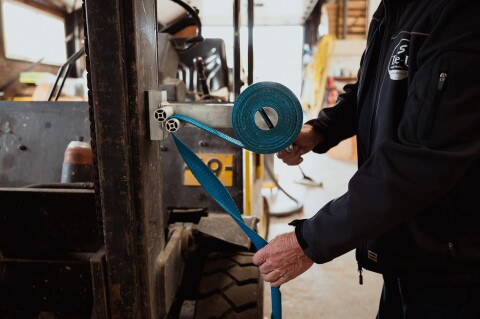 Monteur rolt een oranje spanband strak op met de spanbandoproller op een metalen werkbank.